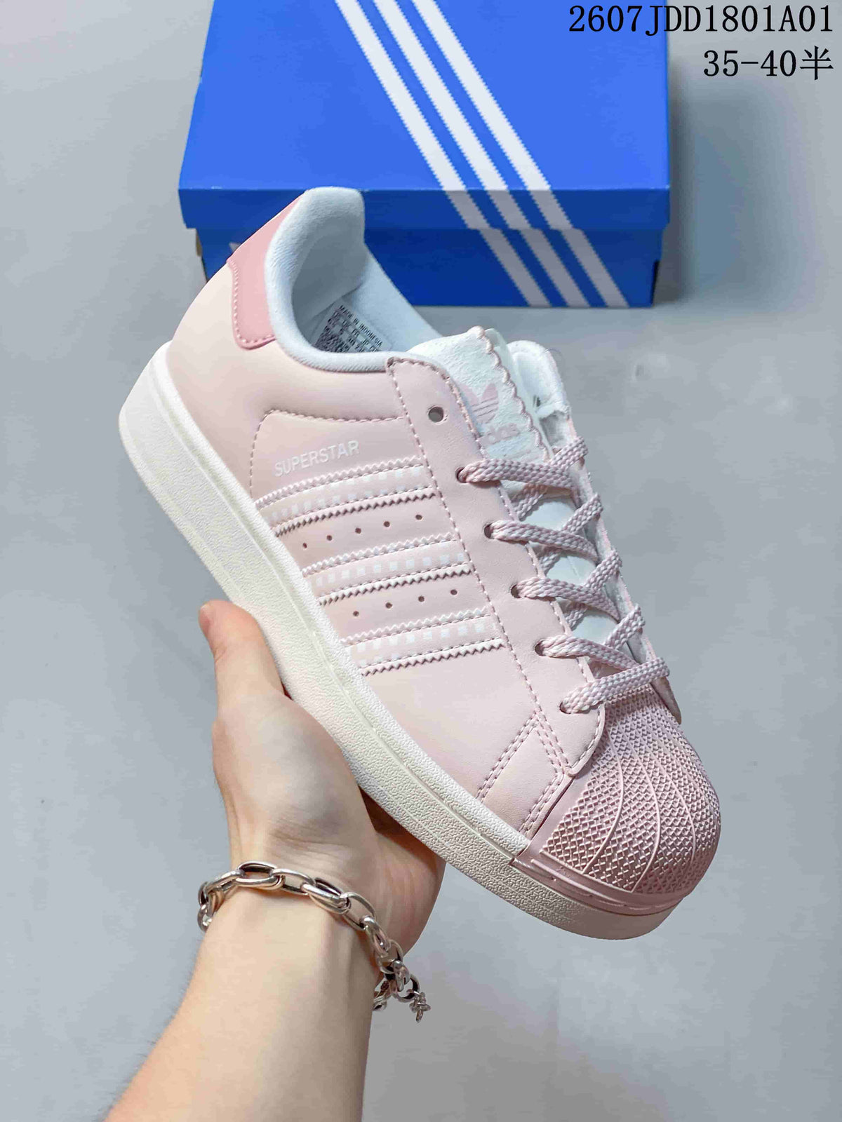 Close-up of a pastel pink Adidas Superstar sneaker showing side stripes and shell-style toe
