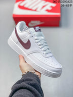 White Nike Court Vision Low sneaker with a burgundy Swoosh and burgundy tongue label.