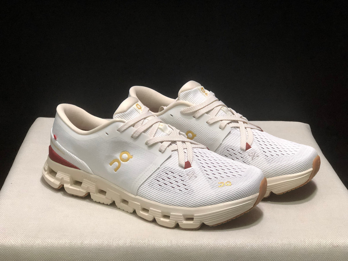 Three-quarter view of the white On Cloud X4 pair highlighting the mesh-like upper, gold branding, and cream outsole.
