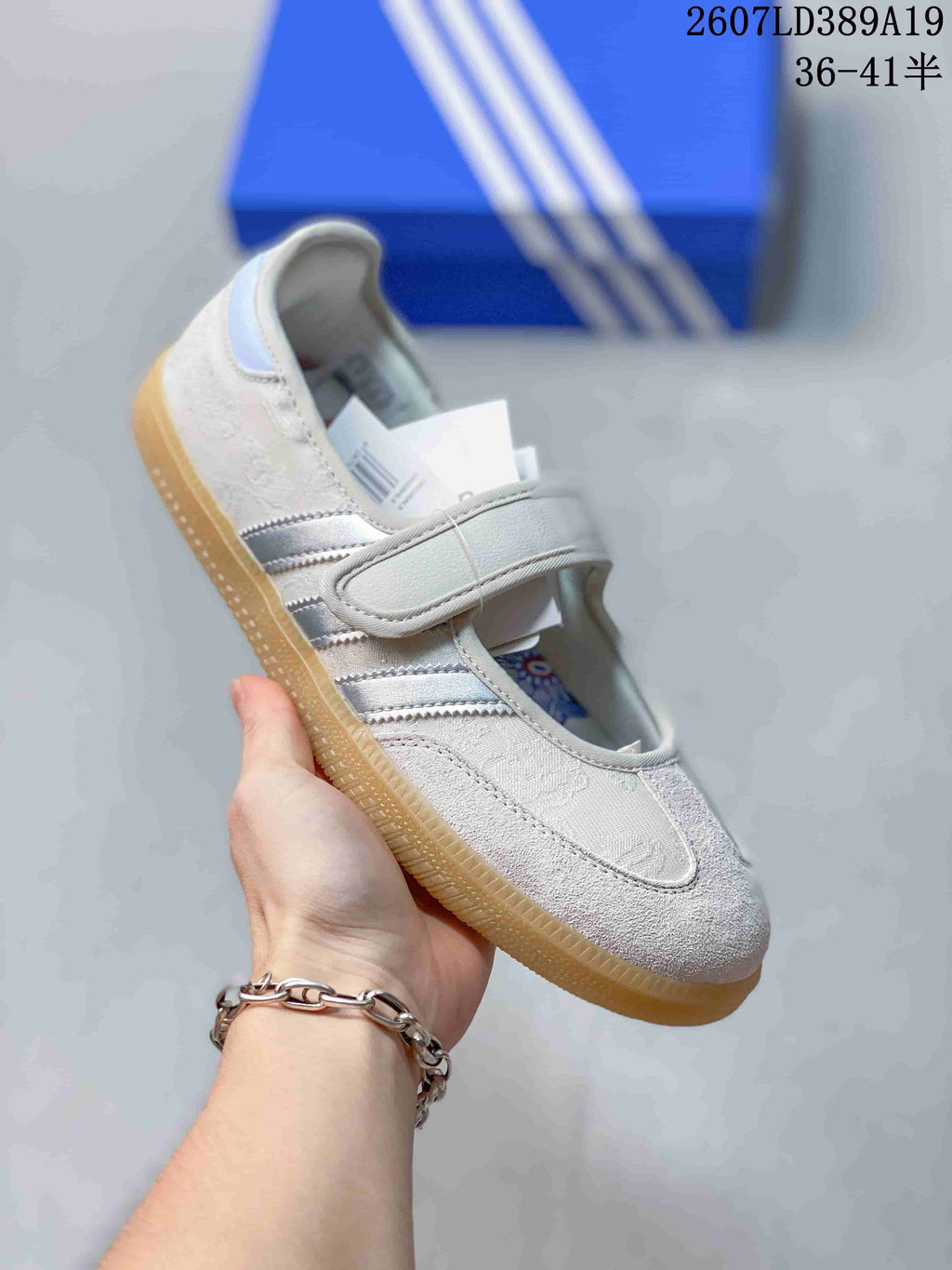 Angled side view showing the white upper, silver stripes, strap closure, and gum-colored sole.