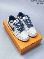 Pair of white sneakers with pale green and gray monogram-style side panels, dark navy collars, and dark navy laces on an orange shoe box.