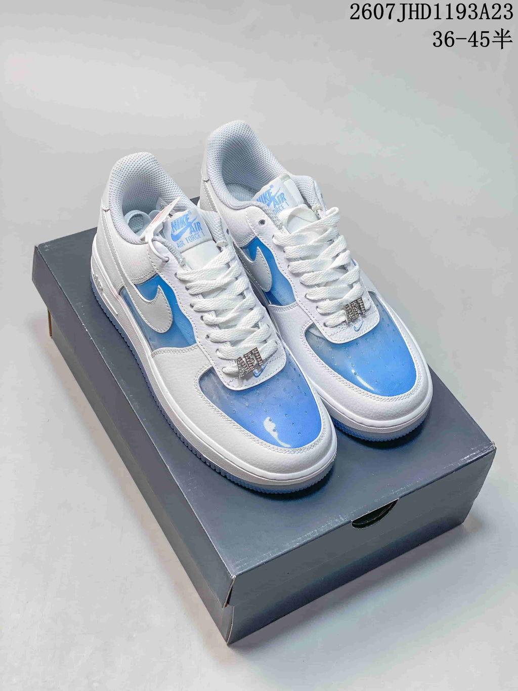 Pair of white and blue Nike Air Force 1 ’07 low-top sneakers displayed on a shoebox; source text shows style code 2607JHD1193A23 and sizes 36–45.