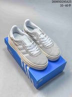 Pair of grey-and-white adidas Gazelle Bold low-top sneakers displayed on a blue adidas shoe box.