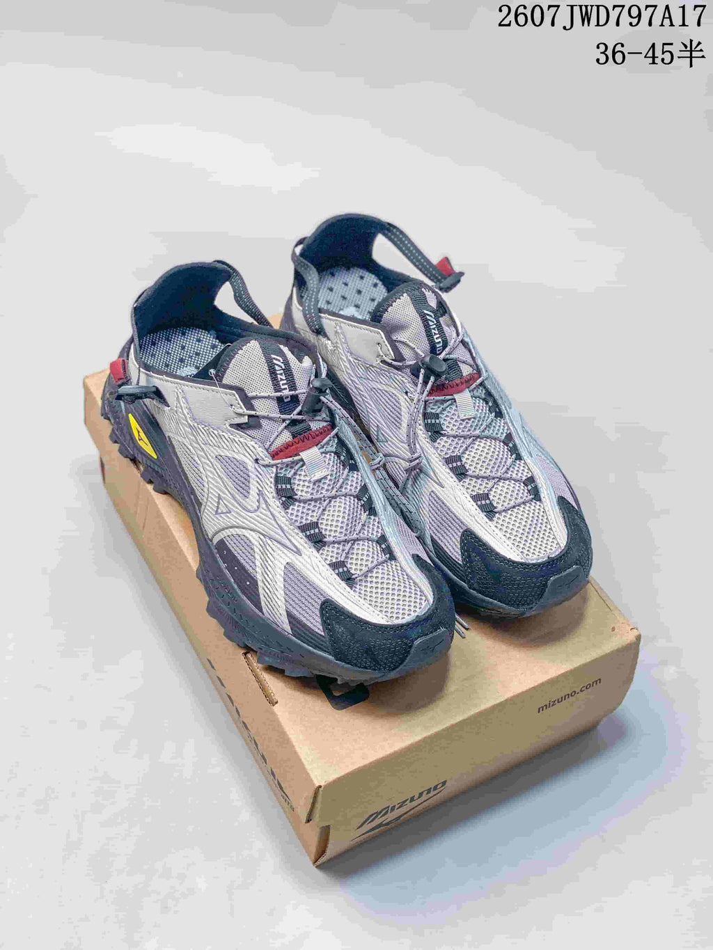 Pair of silver and black Mizuno sneakers displayed on a shoebox; model code 2607JWD797A17 and size range 36–45 are visible.