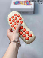 Underside of a cream sneaker showing the textured outsole and contrasting orange circular pods.