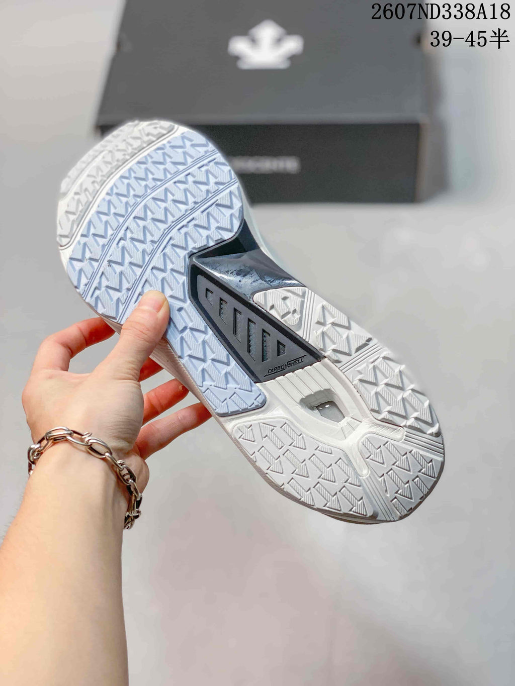 Underside view of the white sneaker showing a geometric traction outsole pattern and central black support section.