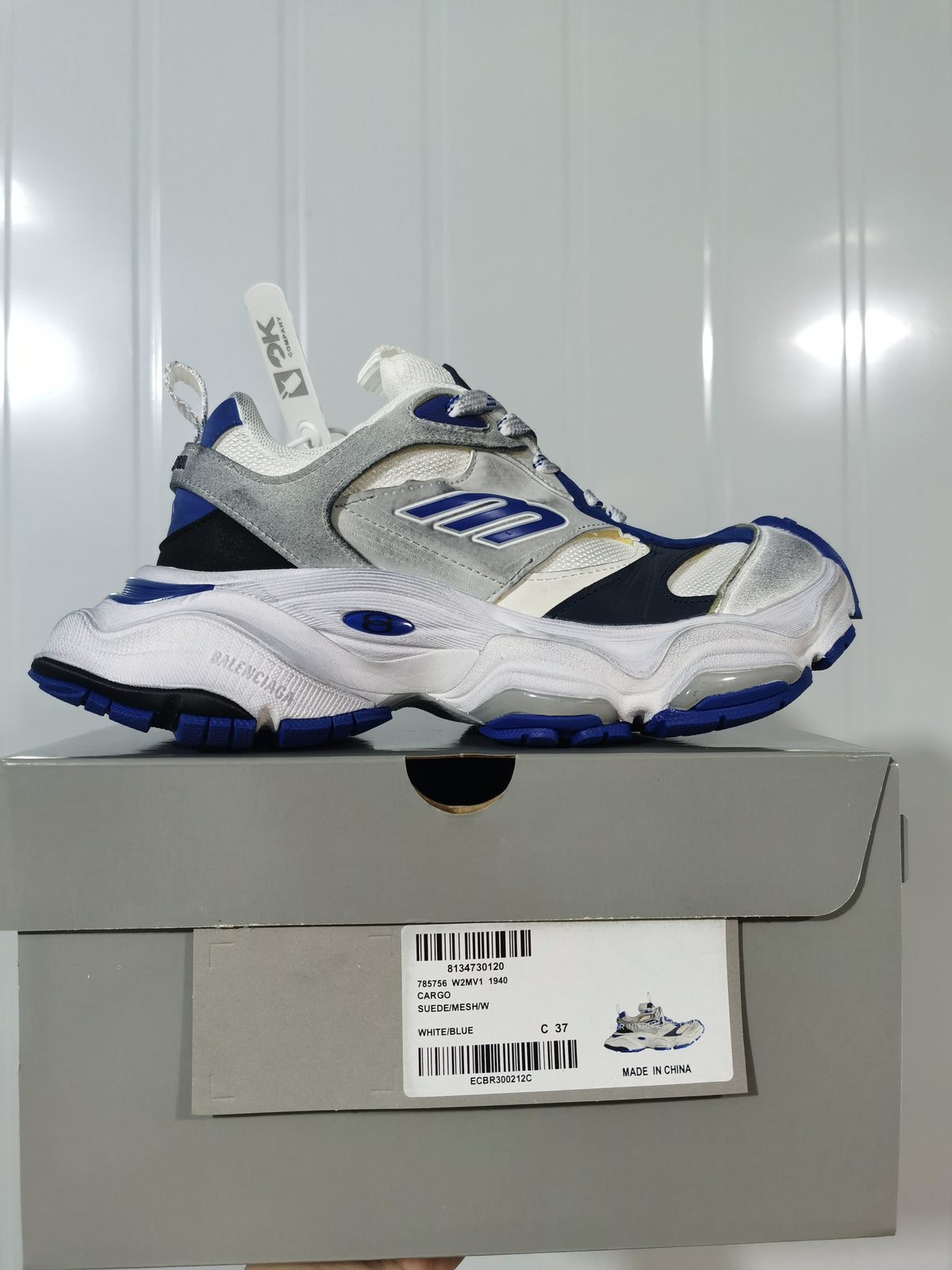 Side profile of the sneaker resting on its box; the box label shows Cargo, style code 785756 W2MV1 1940, White/Blue, and sample size C 37.
