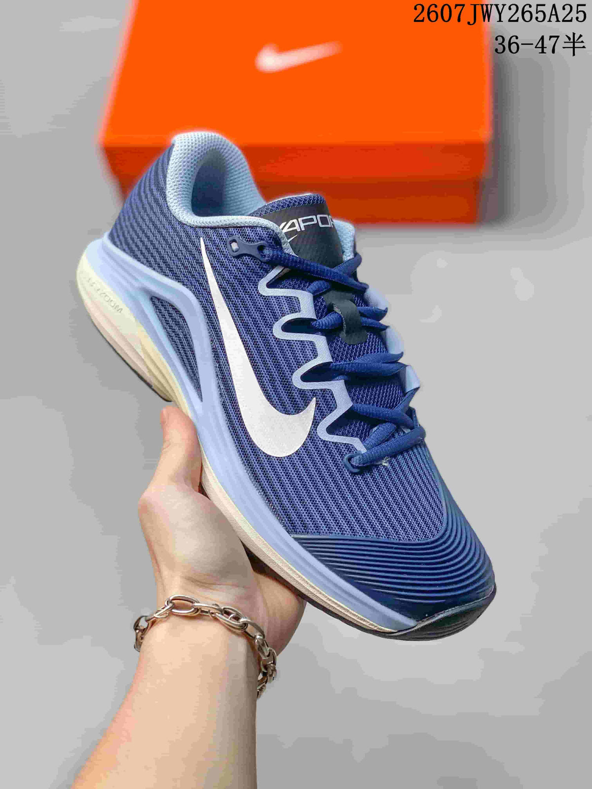 Angled side view of a navy and white Nike Vapor 12 low-top tennis shoe showing the mesh-like upper, side logo detail, and layered sole.