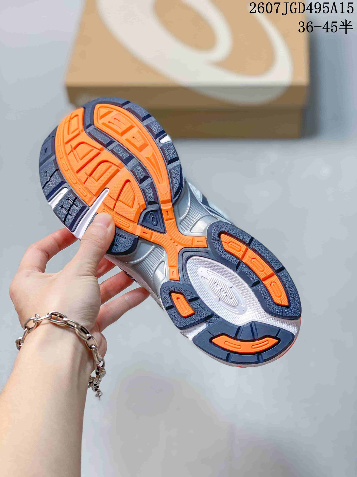Underside view of an ASICS sneaker showing the patterned outsole with orange, navy and gray sections.