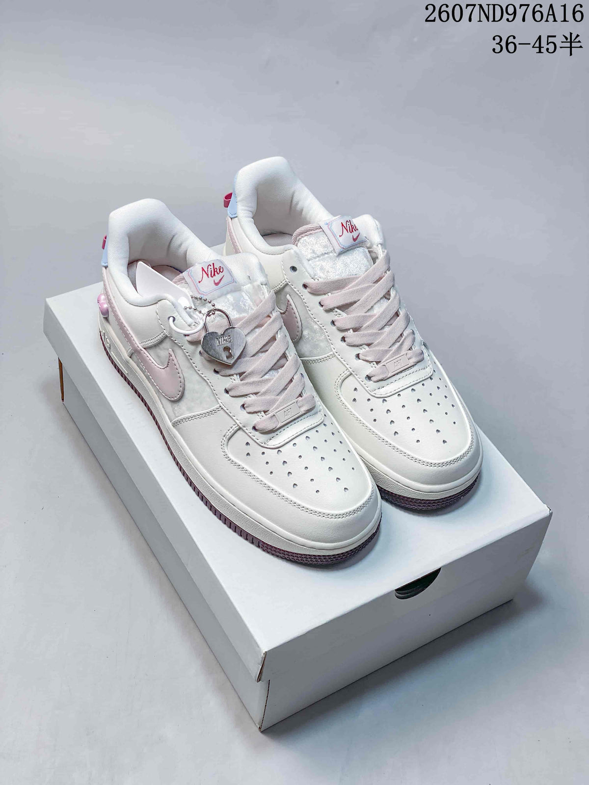 Pair of white Nike low-top sneakers with pale pink accents, decorative charm and code 2607ND976A16 visible above the shoes.