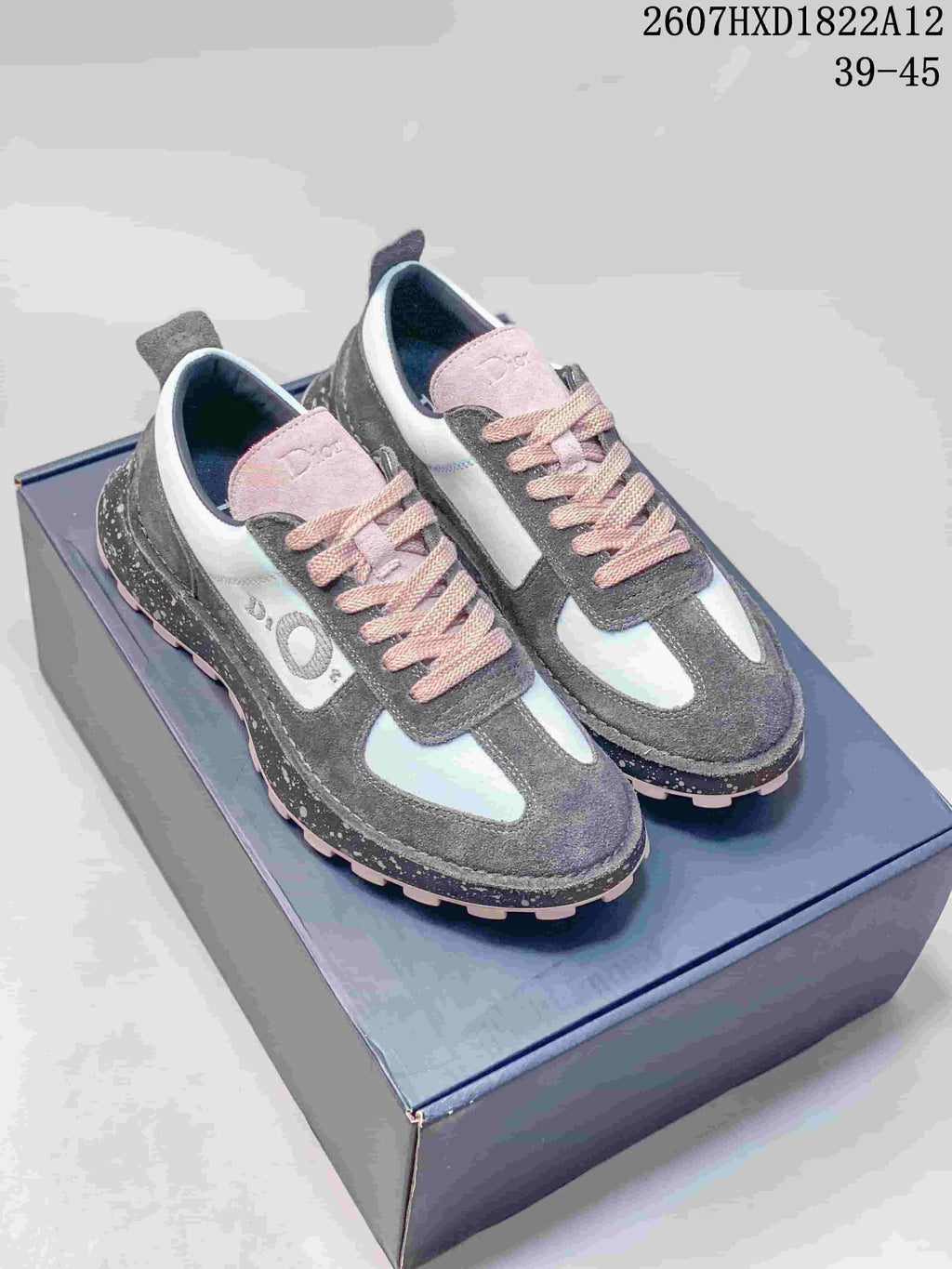 Pair of gray, white, and pink Dior Squash sneakers displayed on a shoebox, showing the pink laces, contrasting panels, and speckled midsoles.