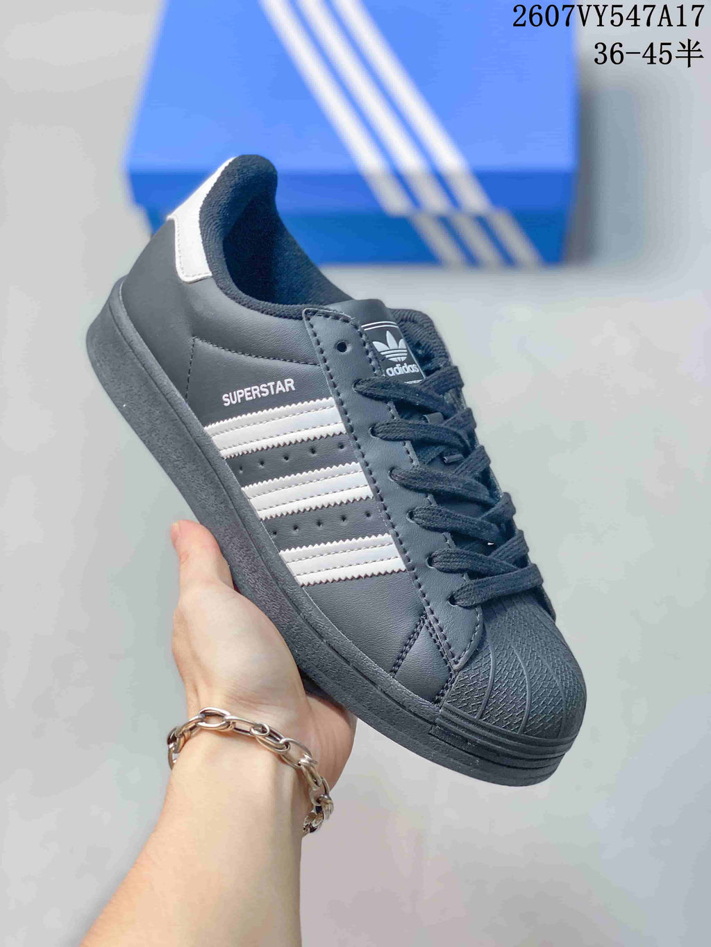 Angled side view of a black Adidas Superstar sneaker showing white stripes, Superstar side branding, and a white heel accent.