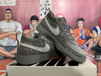 Pair of dark gray camouflage low-top Nike SB Dunk sneakers showing side details and orange outsole accents.