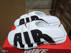 White and black Nike Air-style slide sandals with perforated upper, contrasting panels, and segmented outsole.