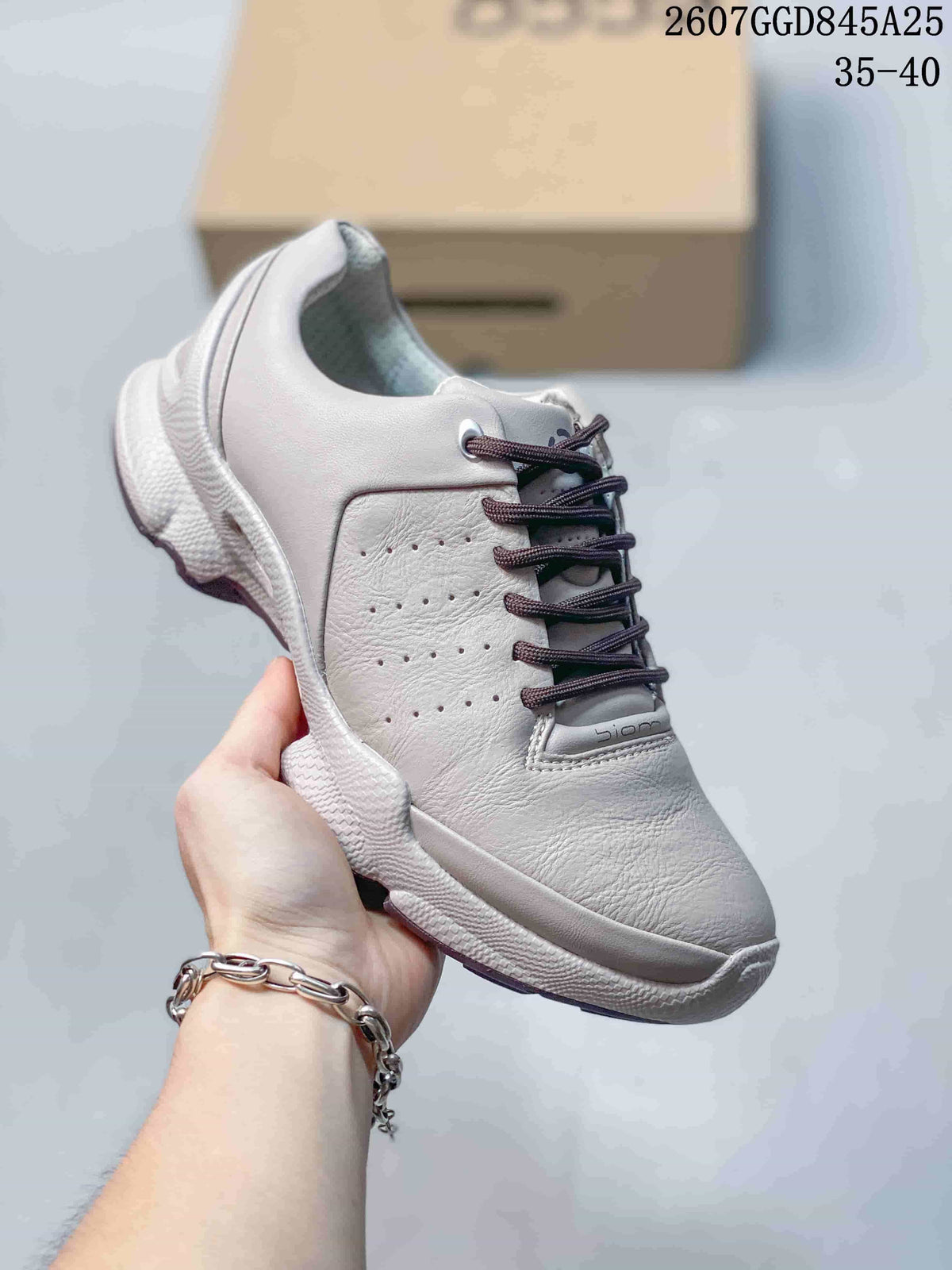 Side view of a white ECCO Biom C sneaker held in hand, showing the padded collar, perforated side panel and layered outsole.