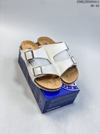 Pair of white two-strap slide sandals displayed on a blue box