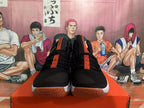 Front view showing black uppers, orange tongue accents, and gum-colored outsoles