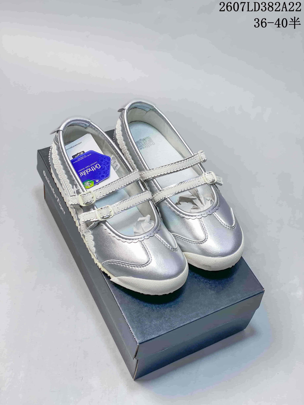 Pair of silver Onitsuka Tiger sneakers displayed on a shoe box, with the source style code and size range visible above.