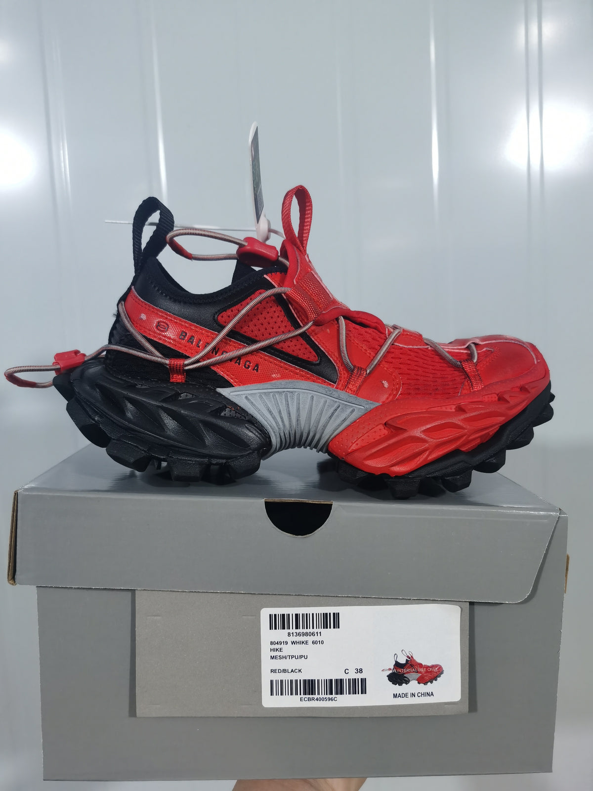 Side view of the red and black sneaker displayed on its box; the box label identifies Balenciaga Hike 6010 in red and black.