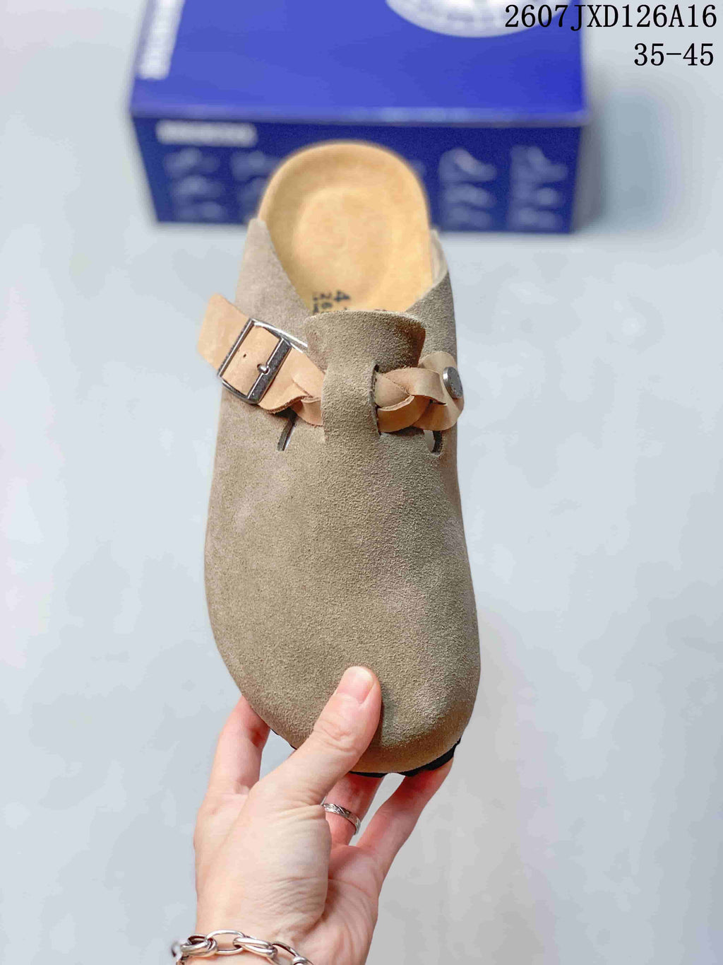 Top view of the rounded closed toe and adjustable buckle strap on the taupe mule; a size marking is visible inside the footbed.