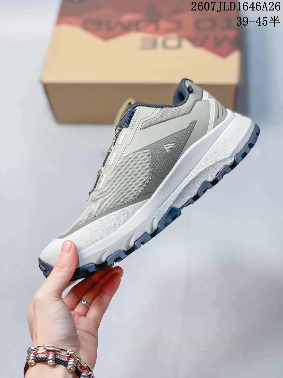 Side profile of the gray low-top outdoor shoe showing mesh-like upper panels, layered overlays, white midsole, and dark outsole.