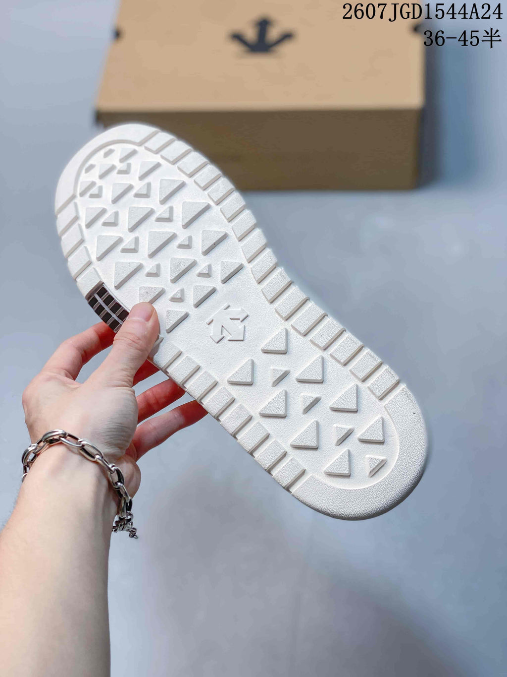Bottom view of the white sneaker showing a textured outsole with repeated geometric tread shapes and a central logo mark.