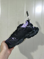 Black and lilac sock-style sneaker shown from the side, highlighting its layered overlays and rugged outsole.