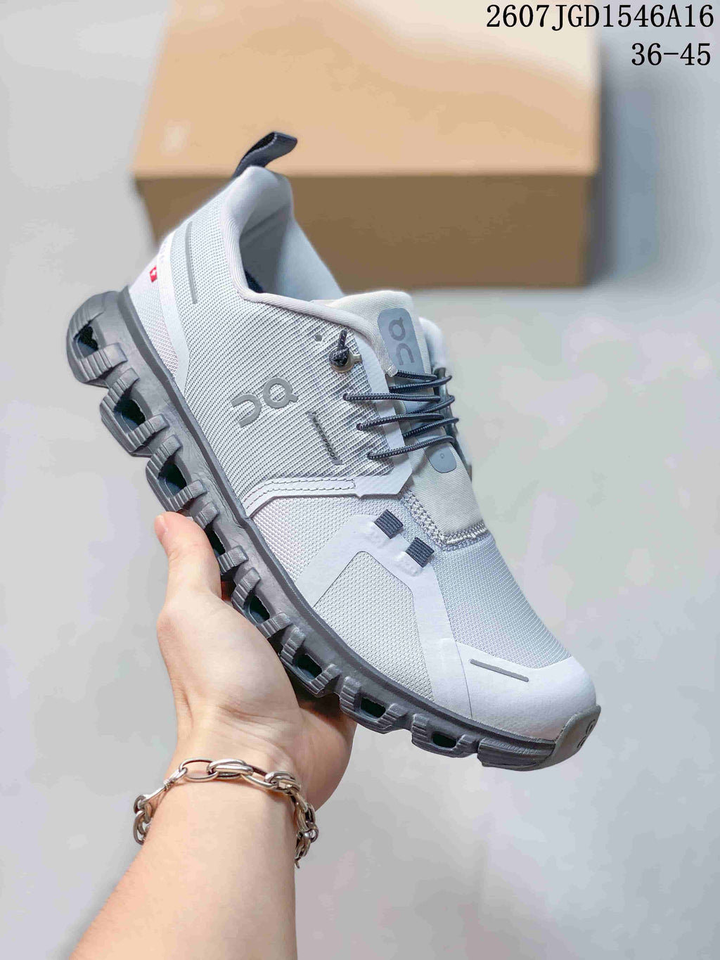 Angled side view of the white and gray sneaker showing the ON side logo, heel pull tab and segmented gray outsole.