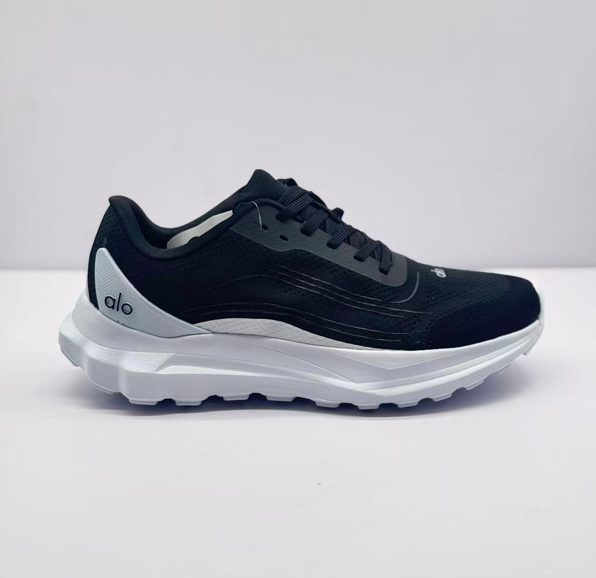 Side view of a black Alo runner sneaker with a white sole and heel panel.