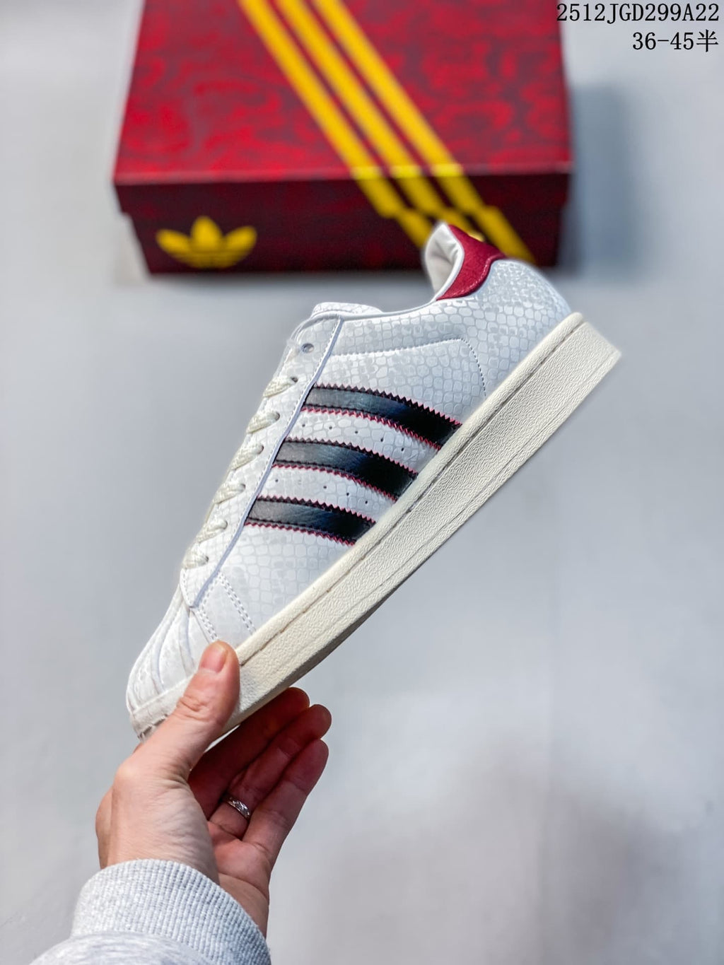Side view showing the white textured upper, black three stripes with red edging, and cream-colored sole.