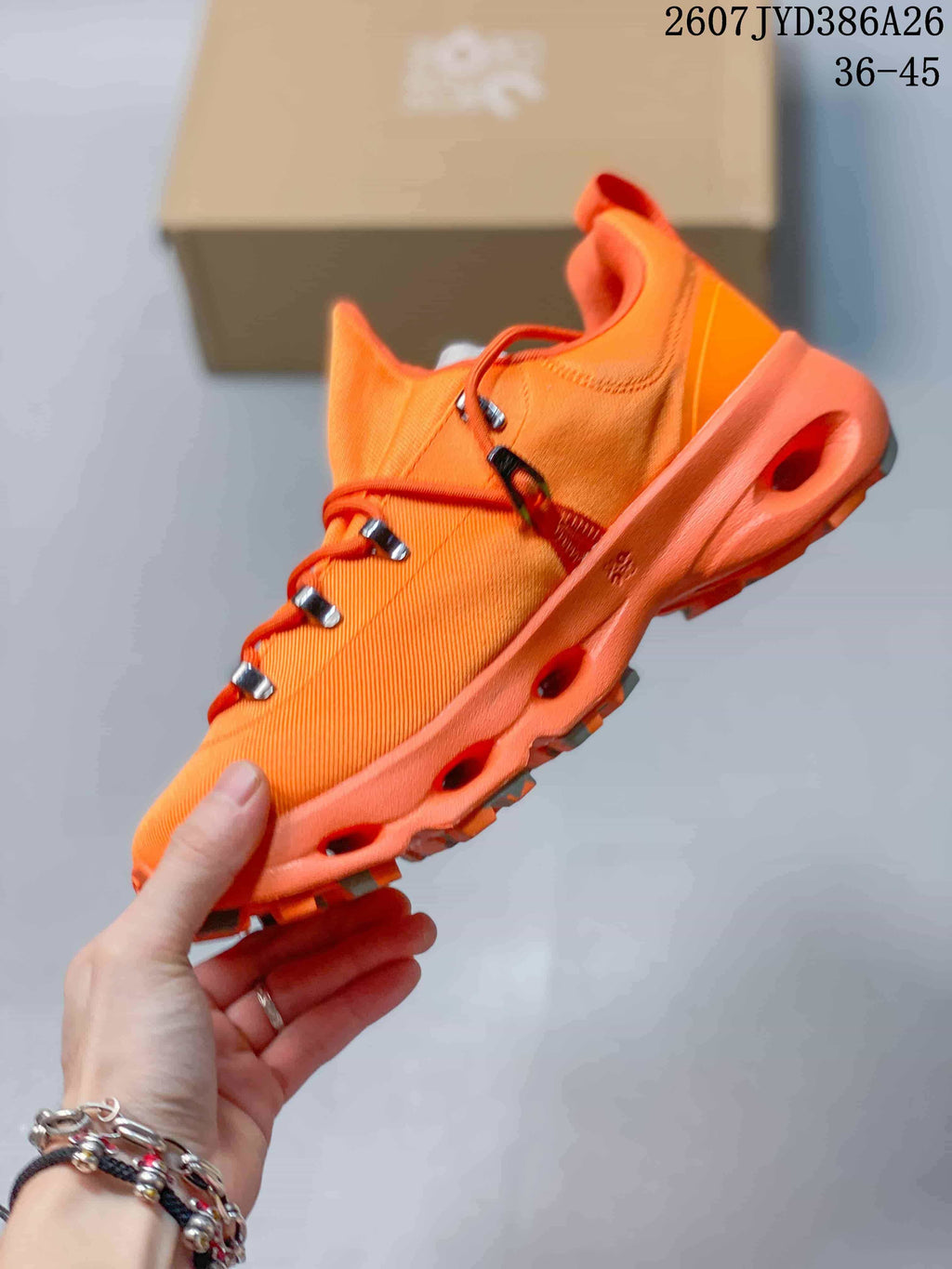 Side view of an orange low-top sneaker showing the textured upper, multi-loop lacing, sculpted midsole, and outsole channels.