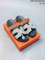 Pair of Hermès Kazimir slide sandals with tan strap accents and light patterned uppers.