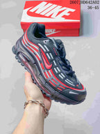 Angled view of a dark gray Nike Air Max TL 2.5 sneaker with red accents and a red shoebox in the background.