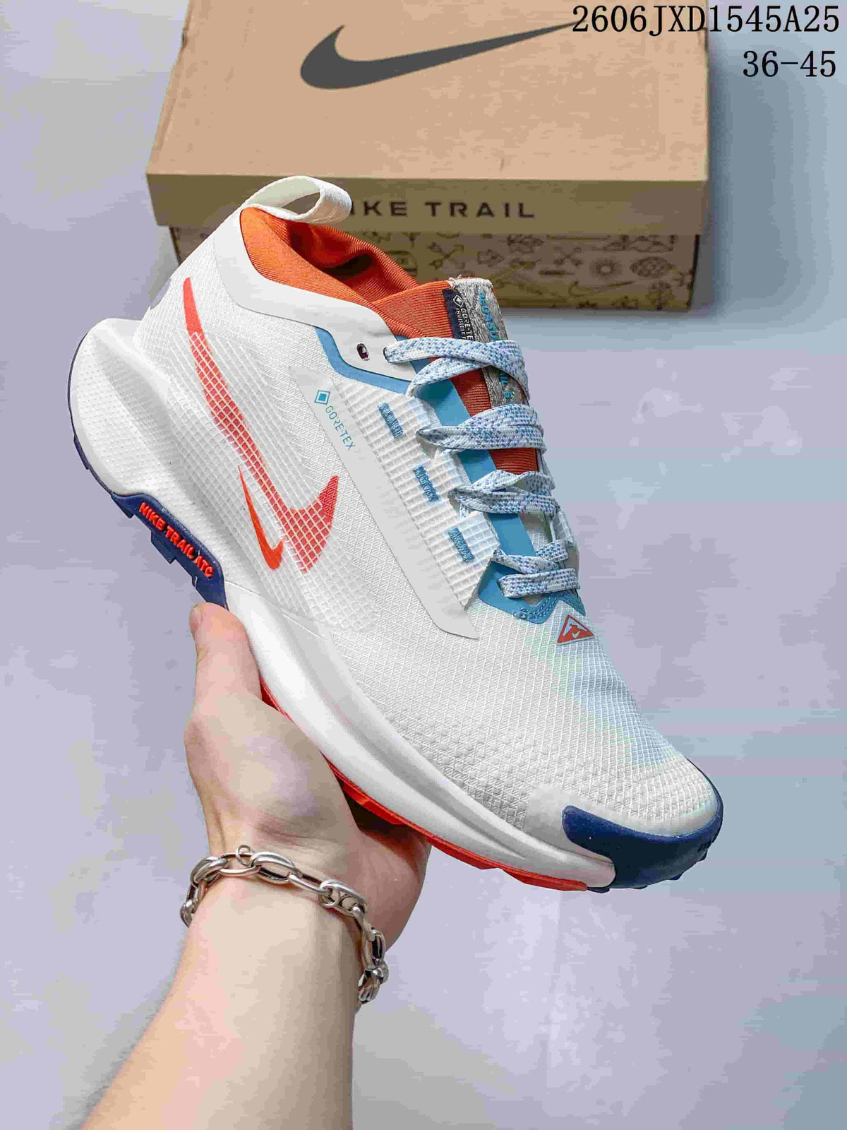 Angled side view of the white Nike trail shoe with orange and blue accents