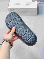 Bottom view of a black sandal showing the wavy patterned outsole and central New Balance logo detail.