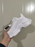 Rear three-quarter view of the white Balenciaga sneaker showing the layered heel, sole accents, laces, and attached tag.