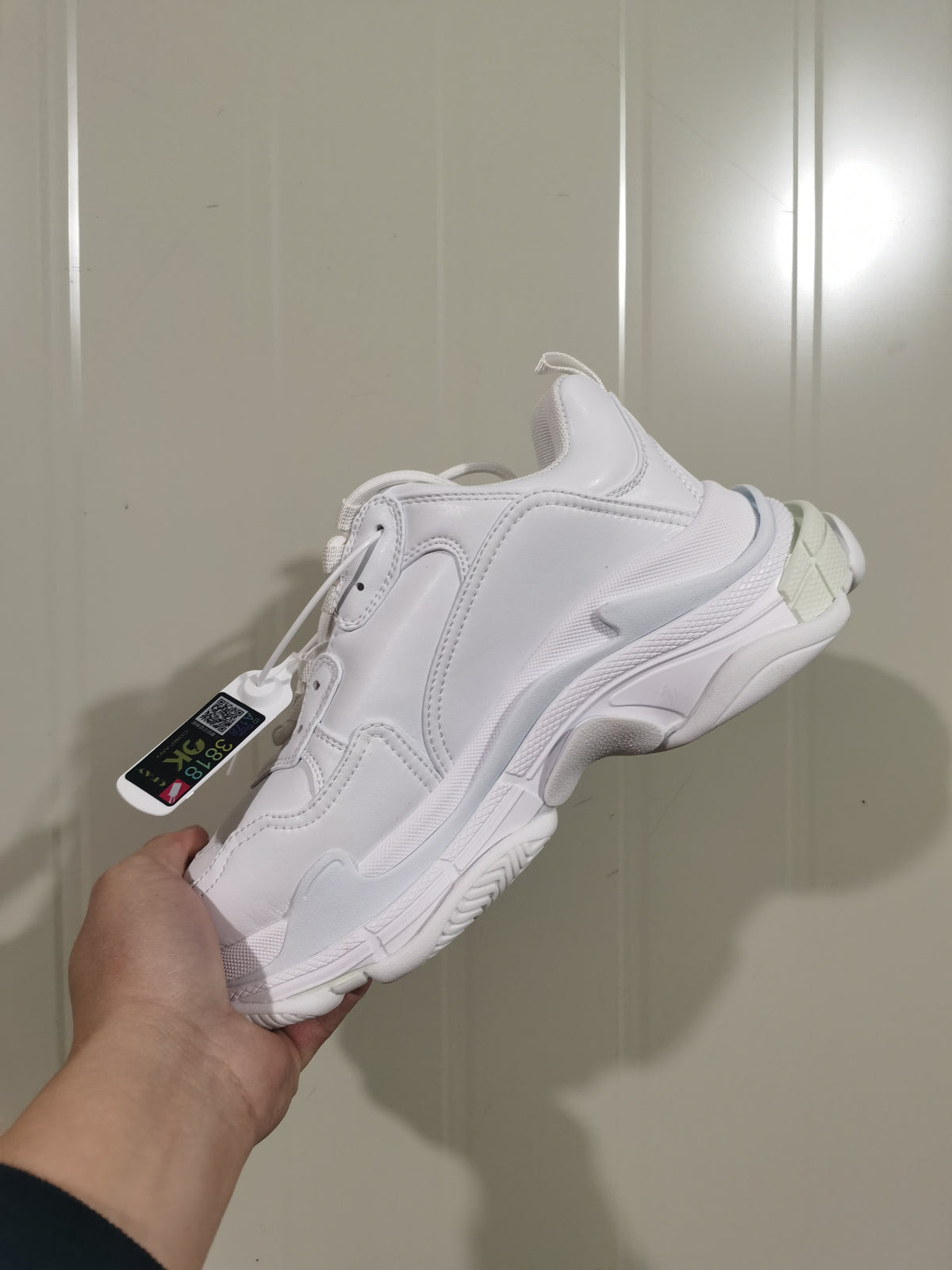 Rear three-quarter view of the white Balenciaga sneaker showing the layered heel, sole accents, laces, and attached tag.