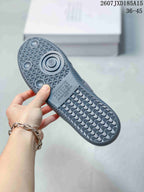 Underside view of a gray sneaker showing the geometric patterned rubber outsole, circular tread details, and printed sole markings.