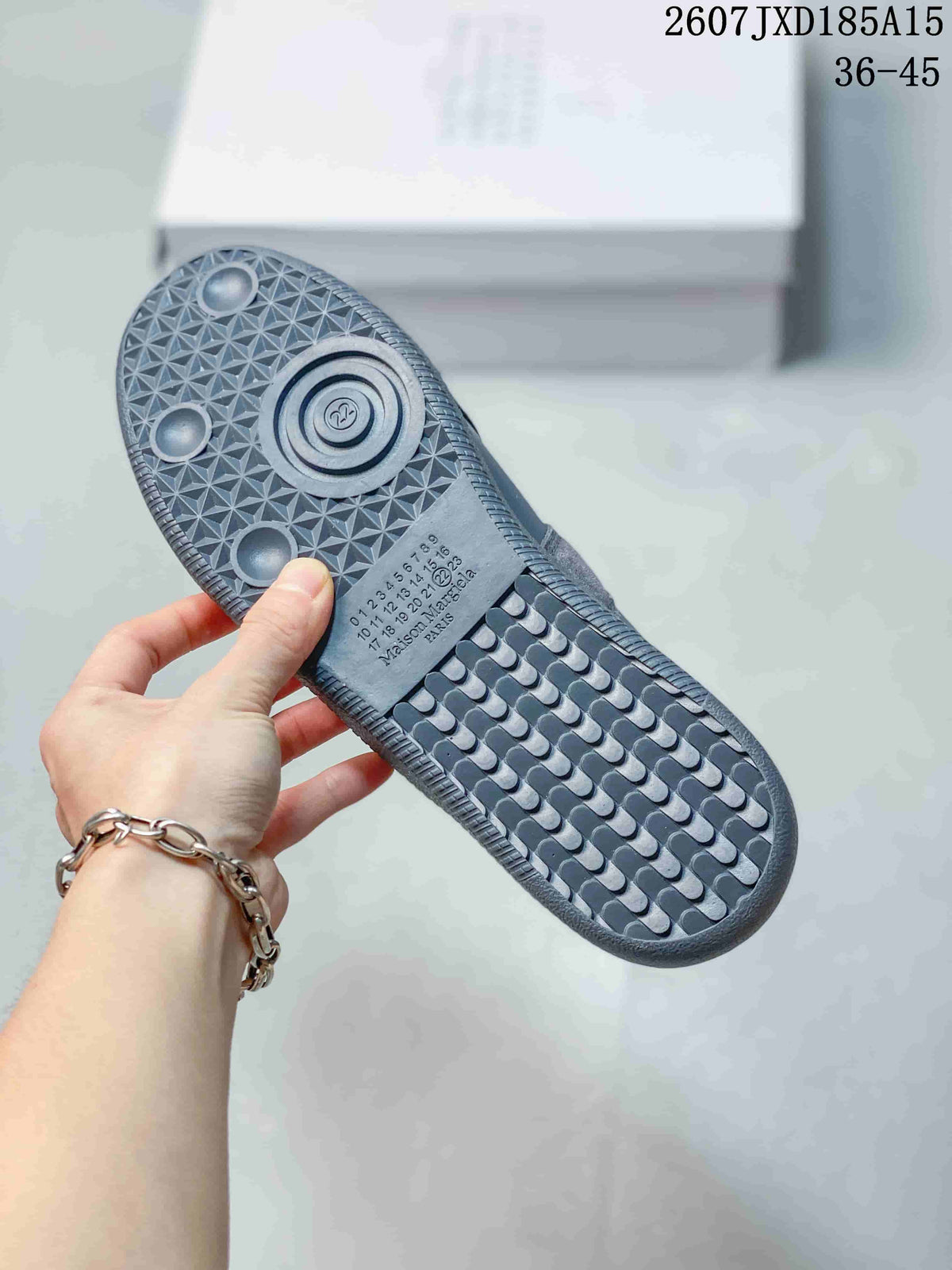 Underside view of a gray sneaker showing the geometric patterned rubber outsole, circular tread details, and printed sole markings.