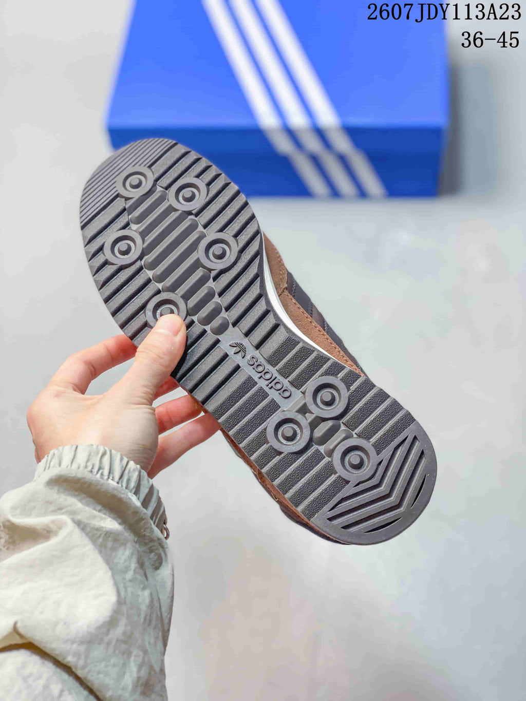 Close view of the dark patterned outsole of a brown adidas sneaker, showing circular tread details and adidas branding.
