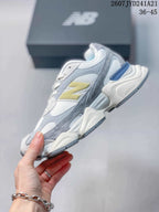 Side view of a New Balance 9060 sneaker showing layered grey and white panels, yellow branding and a sculpted sole.
