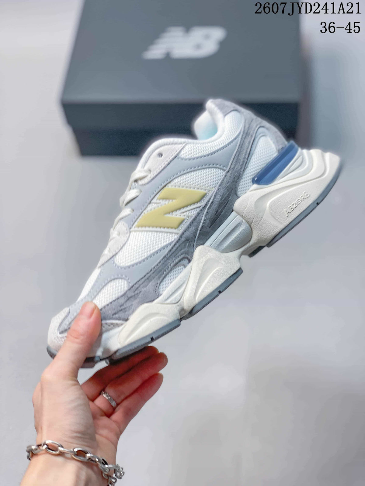Side view of a New Balance 9060 sneaker showing layered grey and white panels, yellow branding and a sculpted sole.