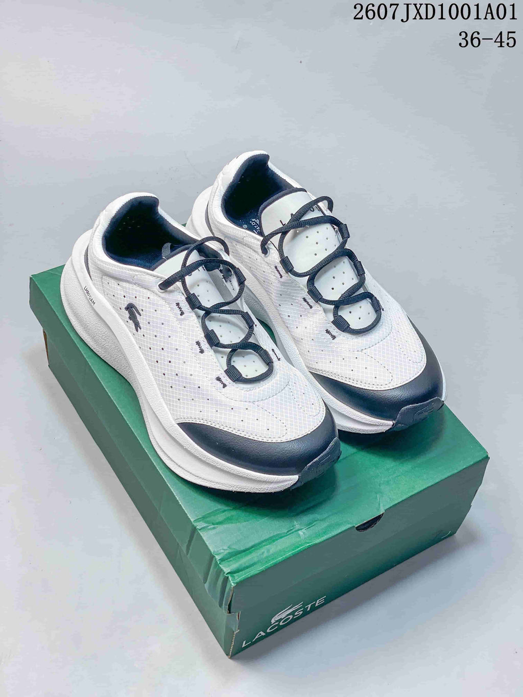White and navy Lacoste sneakers shown from above on a green shoe box