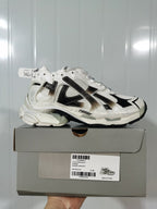 Side-profile product view of the sneaker positioned on its box; the box label shows Runner 9010, White/Black, and size E 40.