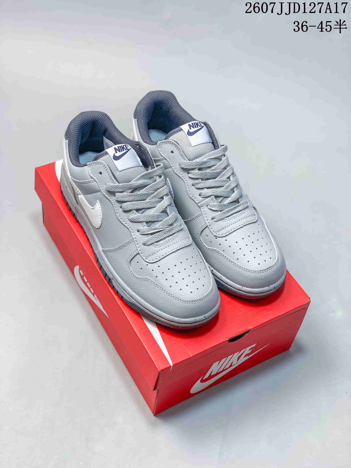 Pair of grey and white Nike SB Dunk Low Pro sneakers displayed on a red shoebox; overlay shows style code JJD127A17 and a size range.