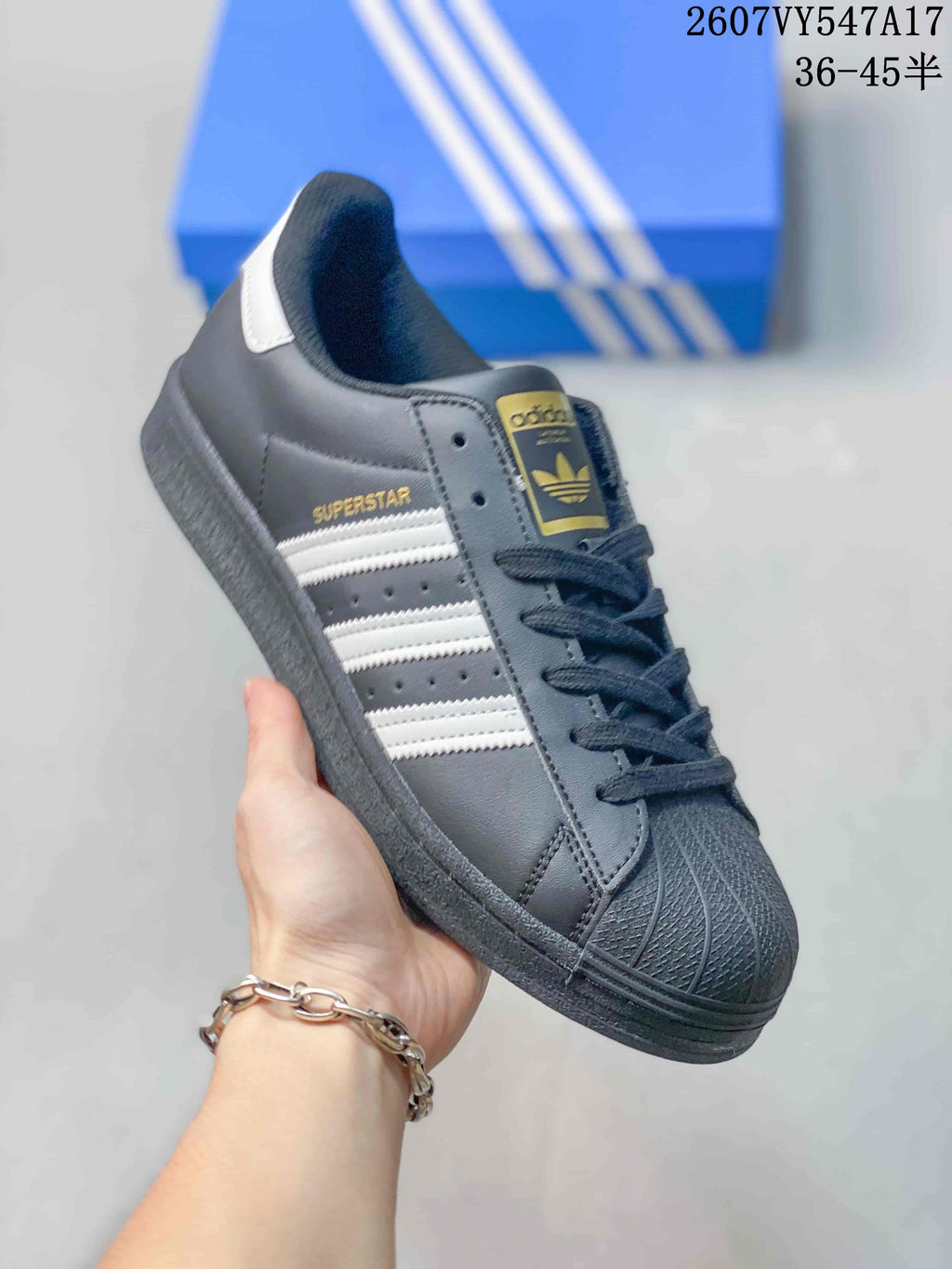 Angled side view of the black Adidas Superstar sneaker with white stripes, gold Superstar lettering and a textured toe cap.