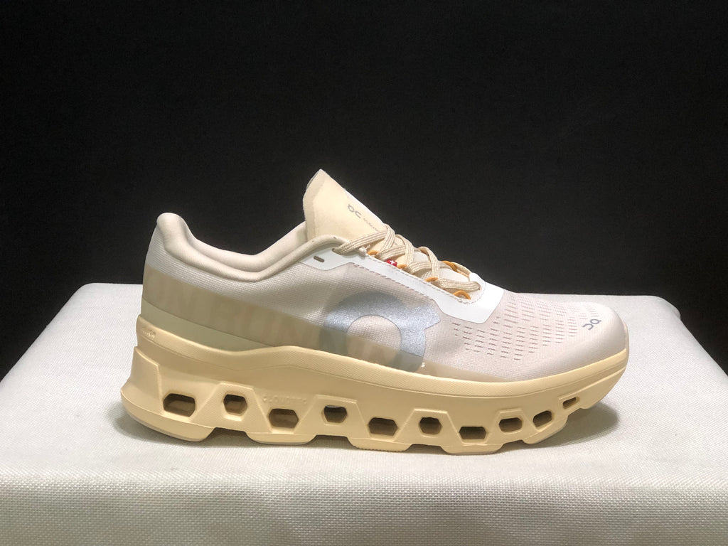Single side profile of the On Cloudmonster 1 sneaker in a light cream and white colorway.