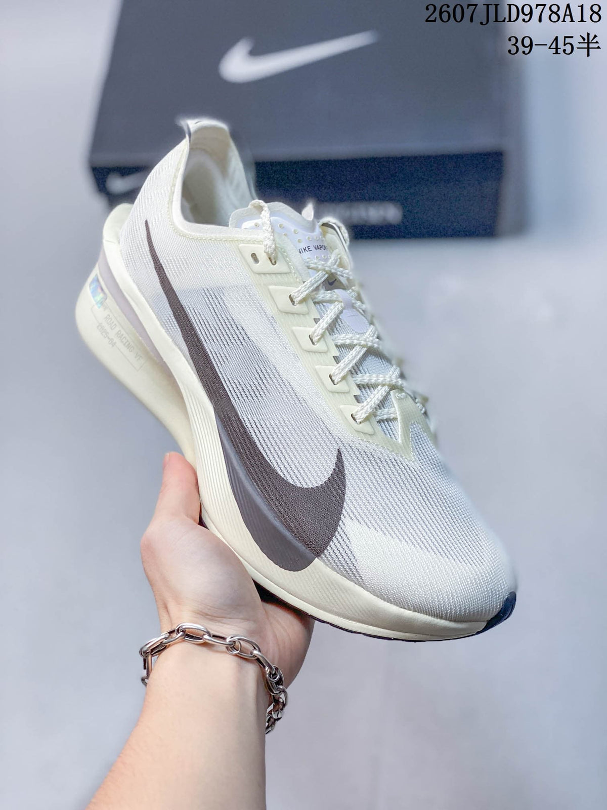 Light-colored Nike racing sneaker with dark side branding and a pale sole accent; image text shows style code 2607JLD978A18 and size range 39–45.