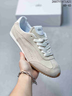 Close side view of a light beige Alo Yoga sneaker showing layered panels, perforated detailing, white laces, and a gum-colored outsole.