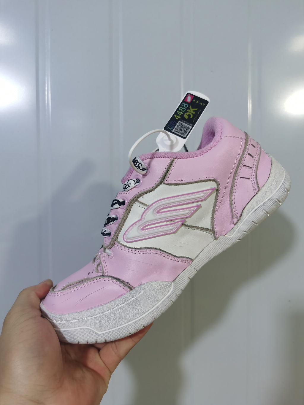 Close-up view of the pink and white sneaker showing the side branding, stitched panels, padded collar, and textured outsole.